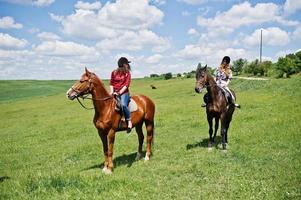 dra unga vackra flickor som rider en häst på ett fält på solig dag foto