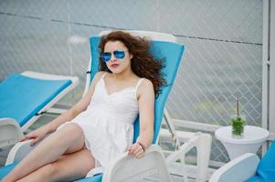 porträtt av en vacker ung kvinna som sitter på en solstol med sina solglasögon på en sjö. foto