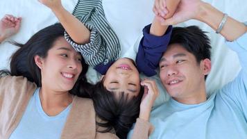 lycklig familjetid, ovanifrån av asiatisk ung mamma, far och barnpojke som ligger tillsammans på sängen i sovrummet med ett glatt och skrattande leende. helg tid föräldraskap med kärlek bra tid att koppla av hemma. foto
