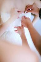 närbild av medhjälpare som hjälper bruden att göra sig redo på sin klänning foto