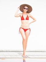 sexig tjej glad tjej i röd bikini bär hatt och solglasögon nära poolen med vit vägg. foto