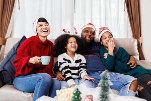 lycklig familj har kul att sitta tillsammans i soffan hemma. glad ung familj med barn som skrattar. afroamerikansk familj foto