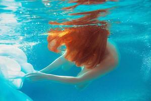 porträtt av leende ung vacker rödhårig flicka i solig dag i öppen pool på sommaren under vattnet foto