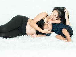 en vacker gravid kvinna som ligger i sängen och tar hand om sin son glatt foto