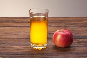 glas äppeljuice och rött äpple på trä