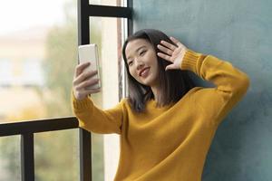 ung asiatisk kvinna som tar selfie och viftar med handen. vacker tonårsflicka foto