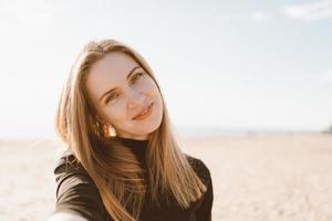 söt kvinna med långt hår tar selfie på smartphone på stranden på sommaren eller hösten. foto