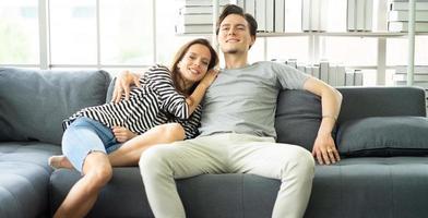 romantiska tillgivna par som omfamnar, sitter på mysig soffa i vardagsrummet kopplar av hemma, bindande förhållande. ung familj porträtt leende överlycklig man och hustru glad fritid tillsammans. foto