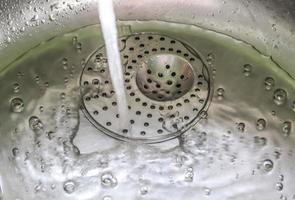 rinnande vatten från en vattenkran till avloppet på ett kromhandfat. foto