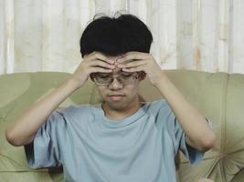 liten asiatisk pojke som bär glasögon med handen på huvudet, huvudvärk på grund av stress. han ledsen med lidande migrän. foto