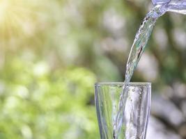 det rena vattnet från kanna i glas på träbord på naturbakgrund. foto