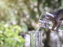 det rena vattnet från kanna i glas på träbord på naturbakgrund. foto