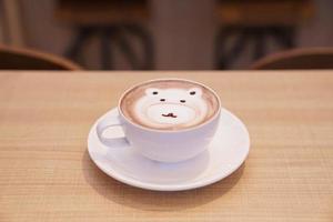 söt björn latte hett kaffe i vit kopp på träbord, läs för att servera. foto