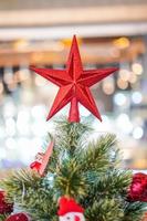 röd stjärna dekoration på tre med oskärpa stor julgran bakom. foto