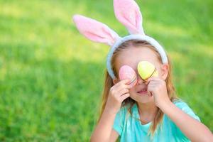 bedårande liten flicka som bär kaninöron med påskägg på vårdagen foto