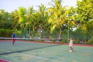 liten flicka spelar tennis med sin pappa på banan foto