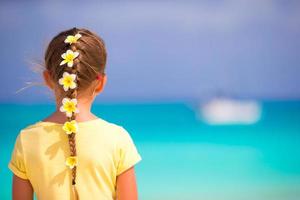 bedårande liten flicka med frangipani blommor i håret på stranden foto