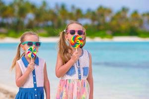 två små flickor som äter ljusa klubbor på stranden foto