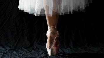 närbild av dansande ben av ballerina som bär vit pointe på en svart bakgrund. foto