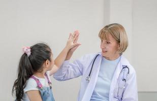 kvinnlig läkare ger high five till en liten söt flicka. barn på konsultation hos barnläkaren. hälsovård och medicin koncept foto