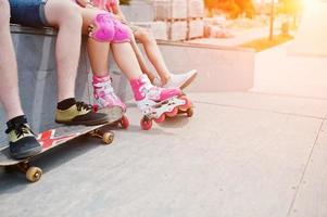 närbild av manliga ben på skateboard och kvinnliga ben i rollerblades och skydd. foto