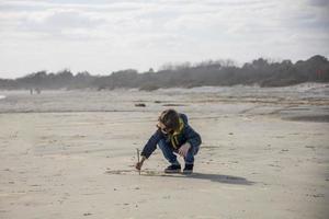 liten flicka ritar på sanden på stranden foto