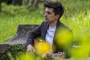 pojke spelar gitarr omgiven av natur foto