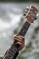 detalj hand spelar gitarr floden bakgrund foto