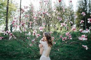 mycket vacker flicka bruden under en slöja, beige bröllopsklänning nära trädet sakura tittar ner, naturen foto