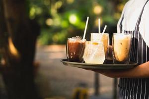 servitör bär förkläde serverar iskaffe en kall drink på en bricka. foto