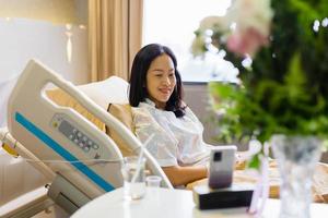 kvinna patient ler och håller en blombukett sitter på sjukhussäng. foto