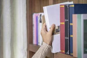 närbild skott hand av ung kvinna tar bok från bibliotekets bokhylla foto