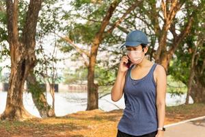 kvinna bär medicinsk mask träning promenader i parken pratar i mobiltelefon. foto