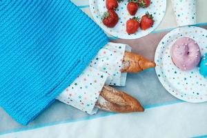 picknickset med jordgubbar, baguette, stickad väska för picknick på pläd foto
