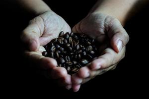 kaffebönor i händerna på hjärtat formad på träbord mörk stil foto