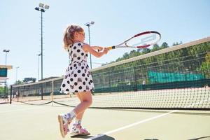 söt liten flicka spelar tennis på tennisbanan utanför foto