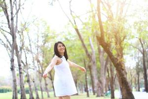 vacker asiatisk kvinna i vit klänning dansar och ler i naturparken. Thai flicka eller kinesisk flicka njuta på semester i trädgården foto