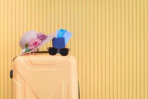 gult hjulbagage placeras i ett rum med bruna trägolv och ljusgula väggar. med en stickad mössa dekorerad med blommor, pass, flygbiljetter och solglasögon för att resa på sommaren foto