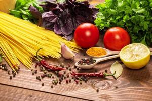 rå pasta, grönsaker, basilika och kryddor på träbordet foto