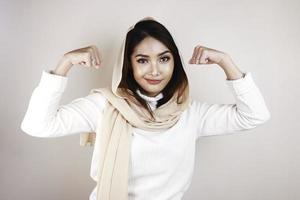 underbara stark ung muslimsk kvinna isolerad över vit bakgrundsvägg visar biceps. foto