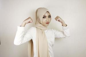 underbara stark ung muslimsk kvinna isolerad över vit bakgrundsvägg visar biceps. foto