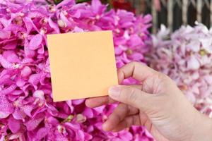 tomt anteckningspapper i handen på vacker lila rosa orkidéblommabukettbakgrund, kopieringsutrymme på kortet för att lägga ditt meddelande. foto
