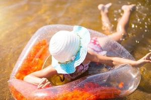 flicka i hatt simmar i floden med en genomskinlig uppblåsbar cirkel i form av ett hjärta med orange fjädrar inuti. havet med en sandbotten. badsemester, bad, solning, solkrämer. foto