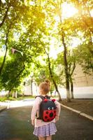 en liten flicka av kaukasiska i en skoluniform med en ryggsäck tittar på vägen på skolgården. koncept tillbaka till skolan. grundskola, utveckla verksamhet för förskolebarn. utrymme för text foto