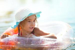 flicka i hatt simmar i floden med en genomskinlig uppblåsbar cirkel i form av ett hjärta med orange fjädrar inuti. havet med en sandbotten. badsemester, bad, solning, solkrämer. foto