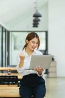 ung kvinna med bärbar dator som uttrycker spänning på hemmakontoret, upphetsad asiatisk kvinna känner sig euforisk när hon läser goda nyheter online. foto