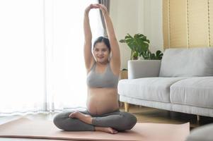 ung gravid kvinna gör yoga hemma, sjukvård och graviditetsvård koncept foto