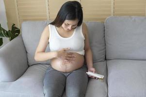 ung gravid kvinna applicerar fuktgivande kräm på mage, sjukvård och graviditetsvård foto