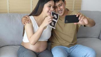 ung gravid kvinna med make som omfamnar och videosamtal med familj och vänner via smartphone på sociala medier, familj och graviditetsvårdskoncept foto