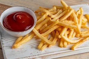 varma gyllene pommes frites med ketchup på en trä bakgrund. välsmakande amerikansk snabbmat. foto
